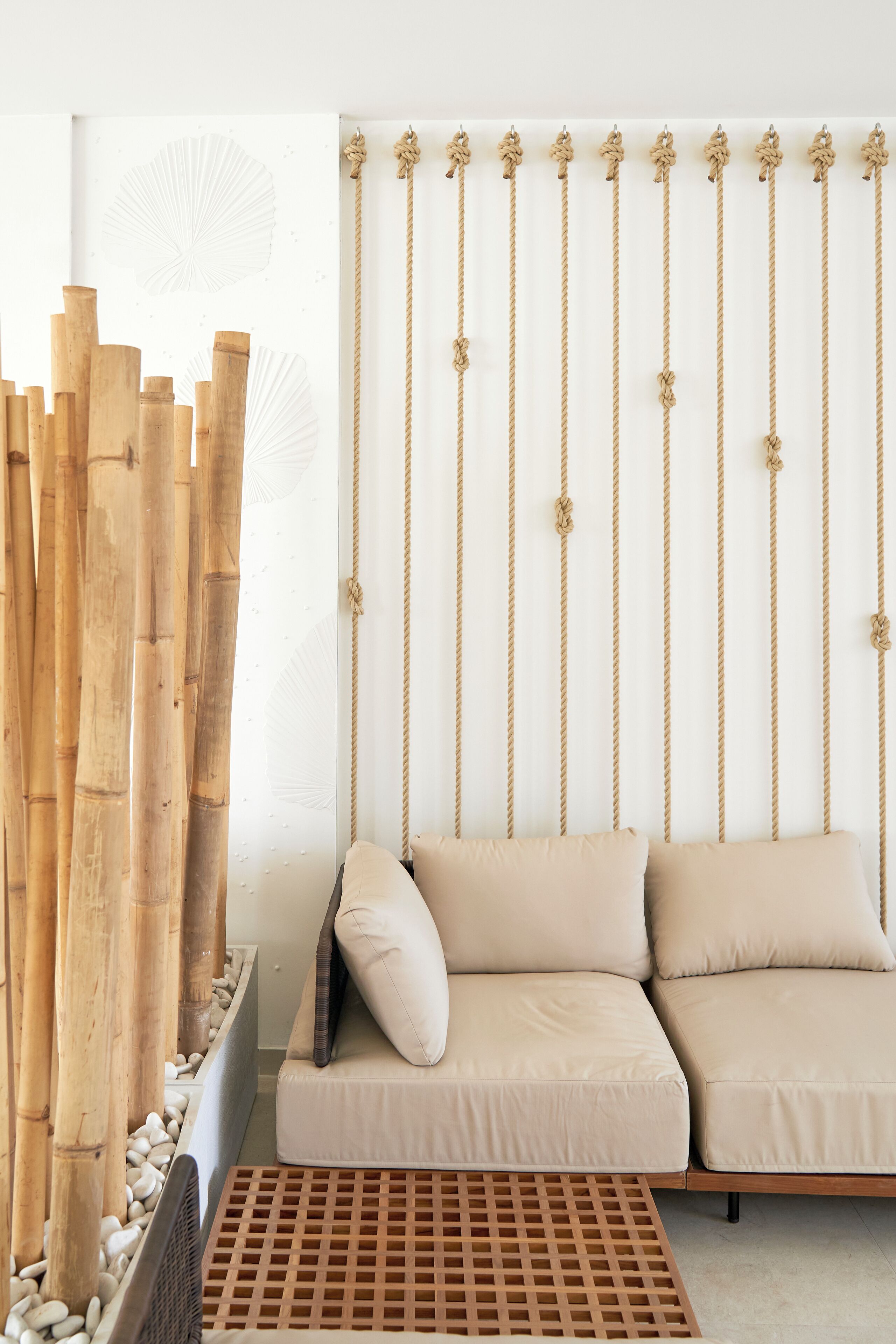 A room with a bamboo screen, a sofa with cushions, and a wall with vertical ropes.