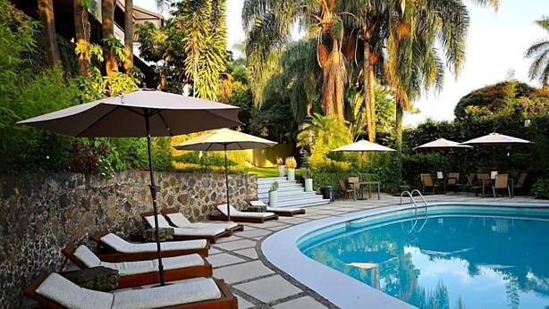A pool area with lounge chairs and umbrellas, surrounded by a stone wall and lush greenery. - Hotel Grand Vista Cuernavaca (Cuernavaca)