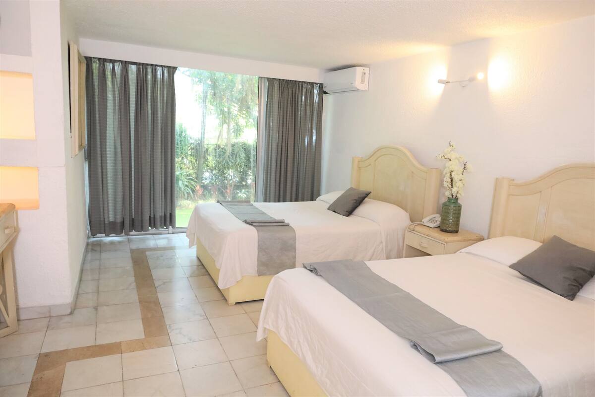 A hotel room with two beds, a nightstand with a phone and a vase, and a window with curtains.