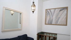 Een kamer met een donkerblauwe bank, een grote spiegel, een houten trap en een lijst met een abstract schilderij.