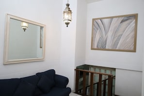 A room with a dark blue sofa, a large mirror, a wooden staircase, and a framed abstract painting. - Hotel Grand Vista Cuernavaca (Cuernavaca)