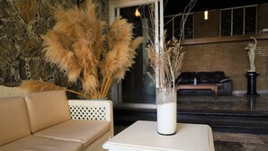 Een kamer met een beige bank, een witte tafel met een vaas gedroogde planten, en een stenen muur.