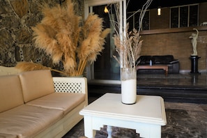 A room with a beige sofa, a white table with a vase of dried plants, and a stone wall. - Hotel Grand Vista Cuernavaca (Cuernavaca)