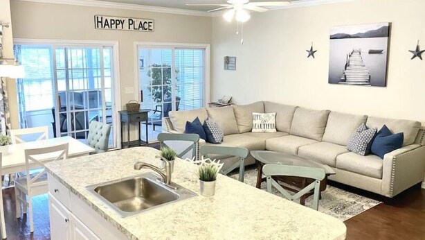 Et moderne køkken med en central ø, et spiseområde med bord og stole, en sofa med puder, og et skilt på væggen med teksten 'HAPPY PLACE'.