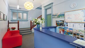 Un espace d’accueil avec un comptoir bleu, un canapé rouge, un vase de fleurs blanches et un tableau blanc contenant des informations sur les voyages.