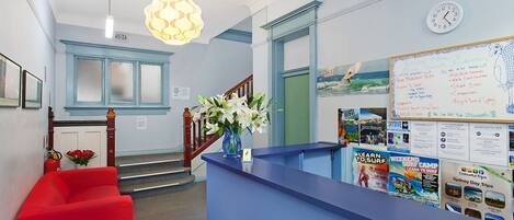A reception area with a blue counter, a red sofa, a vase with white flowers, and a whiteboard with travel information.
