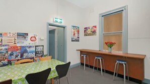 Une pièce avec une table verte, des chaises noires, un comptoir en bois avec des tabourets et des affiches aux murs.