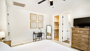 Une chambre à coucher avec un grand lit, un bureau, une chaise, une commode, un téléviseur et un dressing.