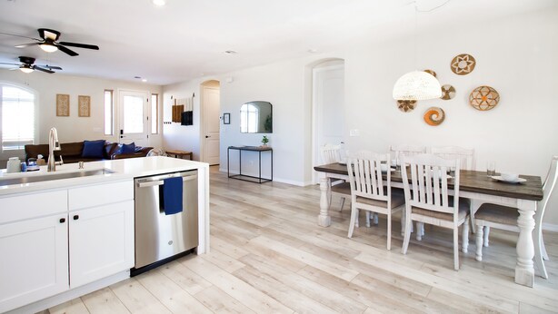 Une cuisine moderne dotée d’un îlot central, d’un coin repas avec des chaises blanches et d’un ventilateur de plafond.