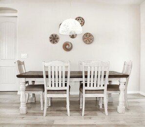 Une salle à manger avec une table et des chaises en bois peintes en blanc, un luminaire suspendu et des assiettes décoratives accrochées au mur.