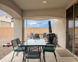 A covered patio with a table and chairs, a grill, and a view of a brick wall and distant mountains.