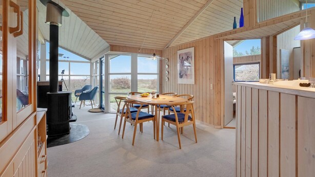 A cozy cabin with a wooden interior, a dining area with blue cushioned chairs, a large window, and a fireplace. - Beautiful home in Thyholm with WiFi (Thyholm)