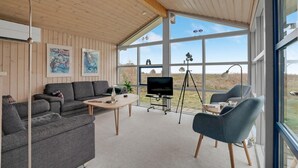 A modern living room with a large window, a sofa, a coffee table, and a TV. - Beautiful home in Thyholm with WiFi (Thyholm)