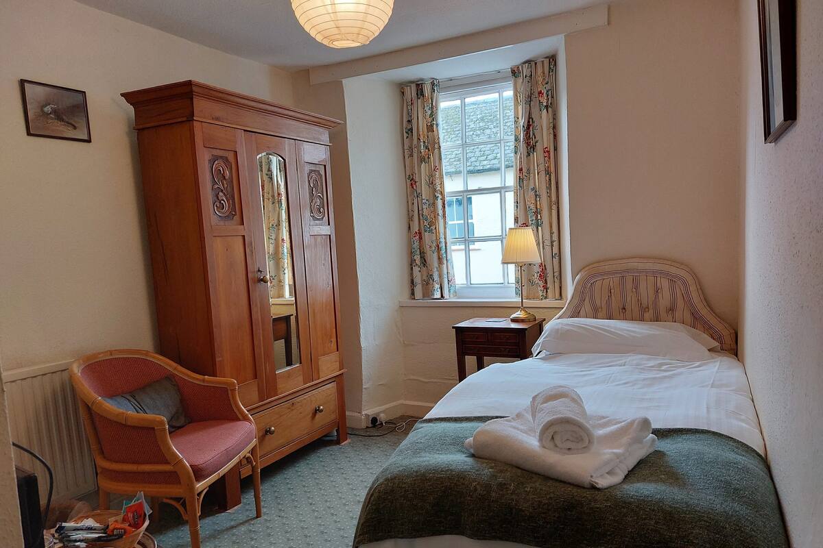 Een slaapkamer met een bed, een houten kledingkast, een stoel, een raam met gordijnen en een bedlamp.