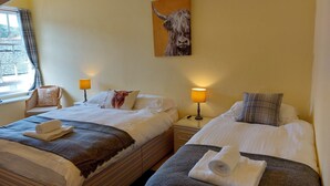 Ein Hotelzimmer mit zwei Betten, einem Fenster mit Vorhängen, einer Lampe und einem Gemälde eines Stiers an der Wand.