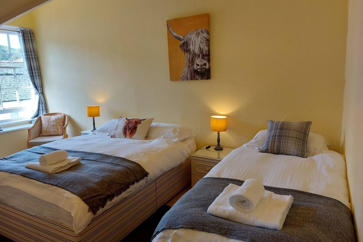 Een hotelkamer met twee bedden, een raam met gordijnen, een lamp en een schilderij van een stier aan de muur.