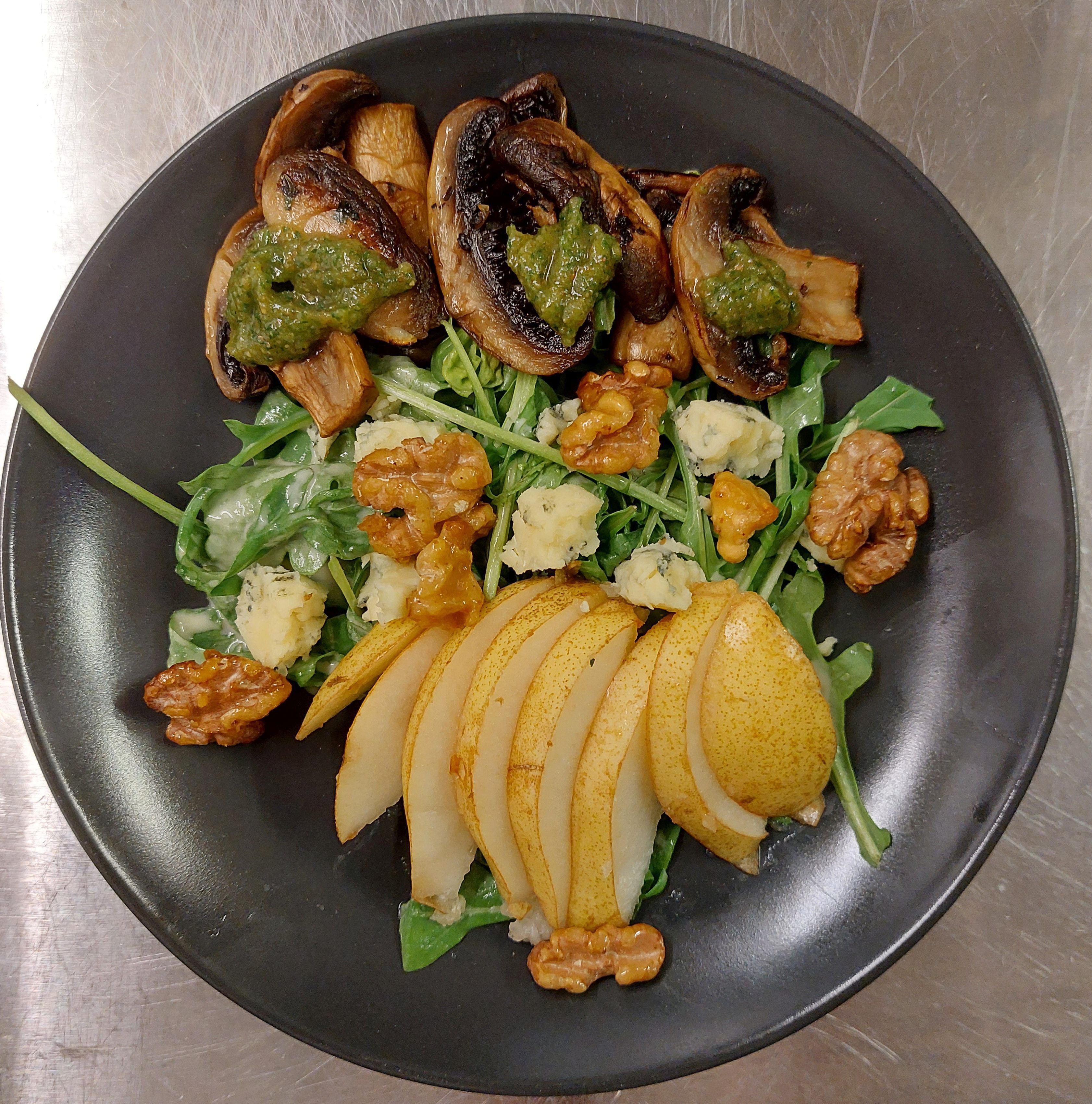 Prato com fatias de pera, nozes e salada de folhas verdes e queijo.