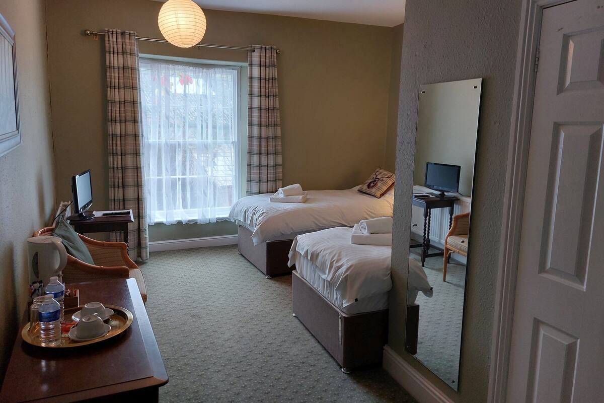 Een hotelkamer met twee bedden, een bureau met een computer, een dienblad met waterflesjes en een grote spiegel.