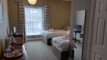 A hotel room with two beds, a desk with a computer, a tray with water bottles, and a large mirror.