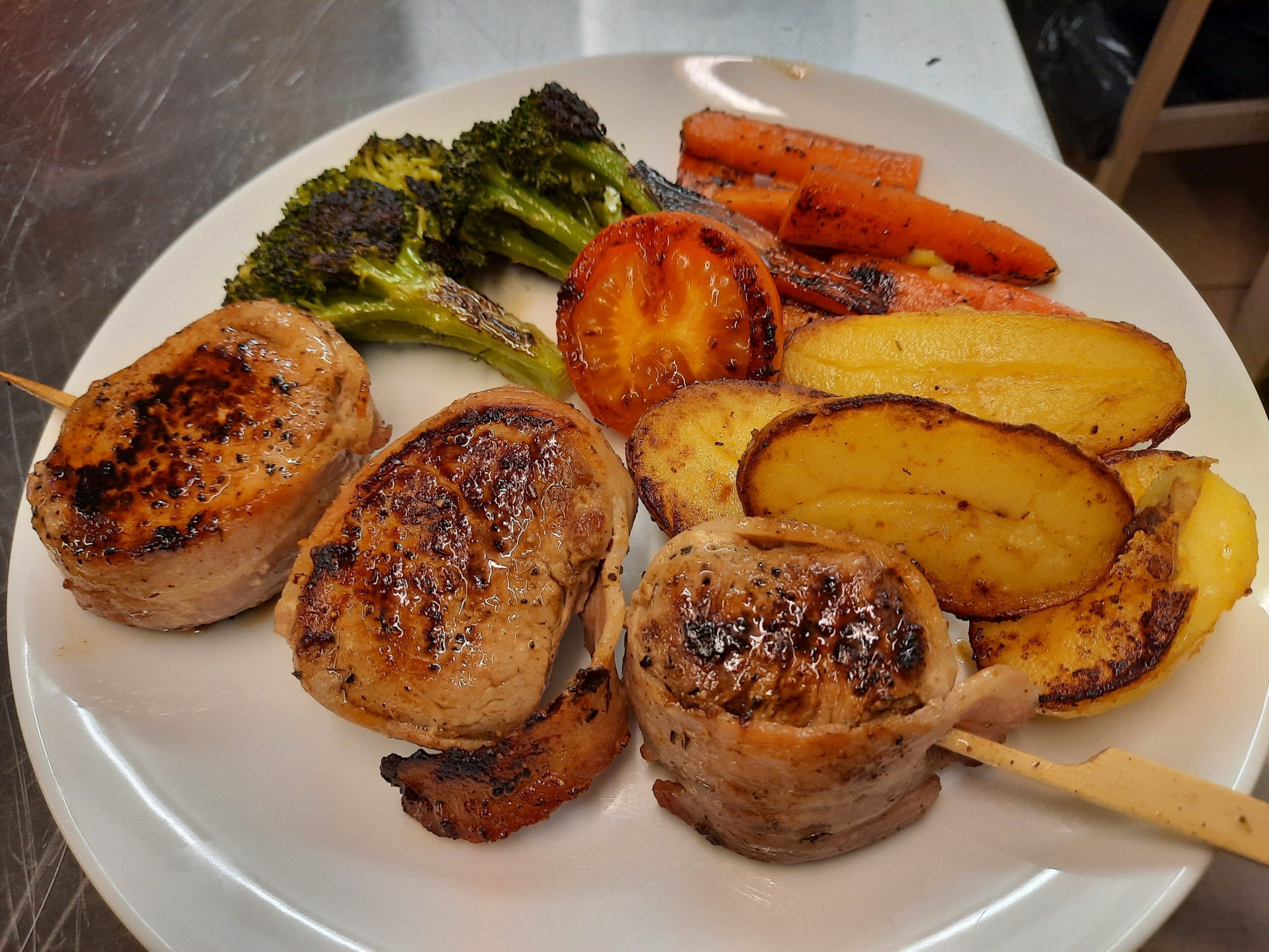 Une assiette composée de viande grillée, de légumes rôtis et de pommes de terre.