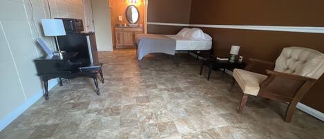 A hotel room with a bed, a chair, a desk with a lamp, a TV, and a bathroom with a mirror and sink.