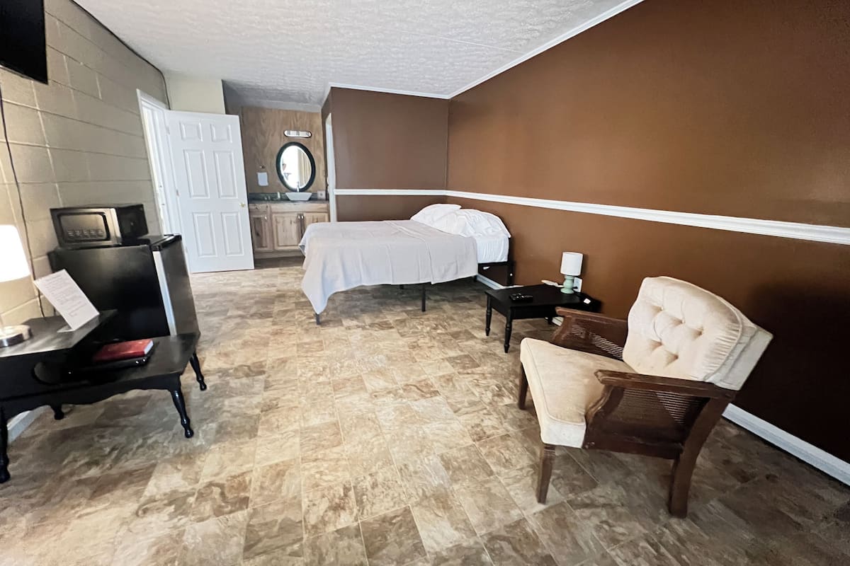 A hotel room with a bed, a desk with a lamp, a chair, and a small table.