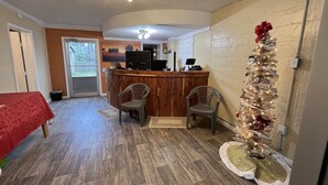 A reception area with a wooden counter, two chairs, a red table, a Christmas tree, and a door leading outside. - Falls of Rough Motel (Falls of Rough)