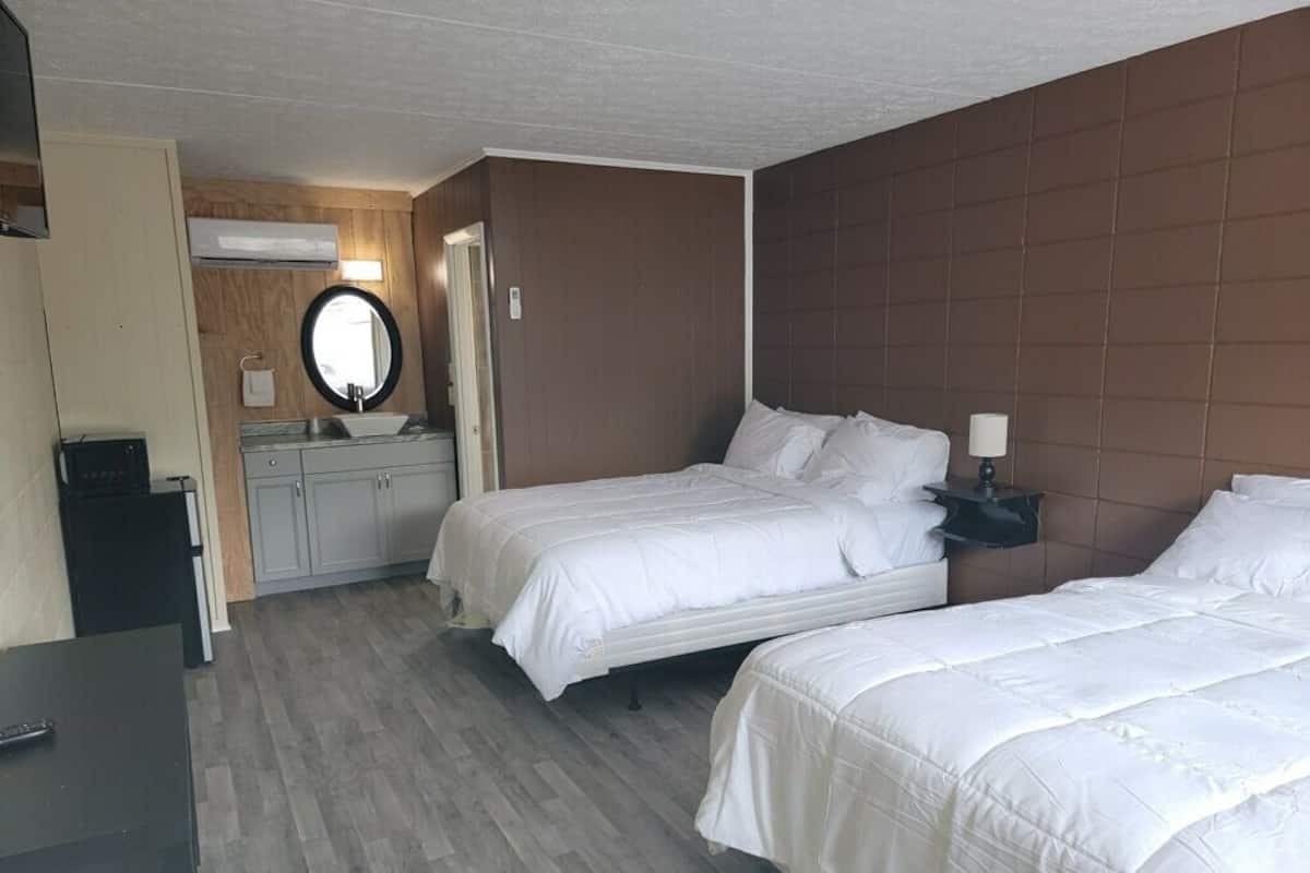 A hotel room with two beds, a desk, a mirror, and a small table with a lamp.