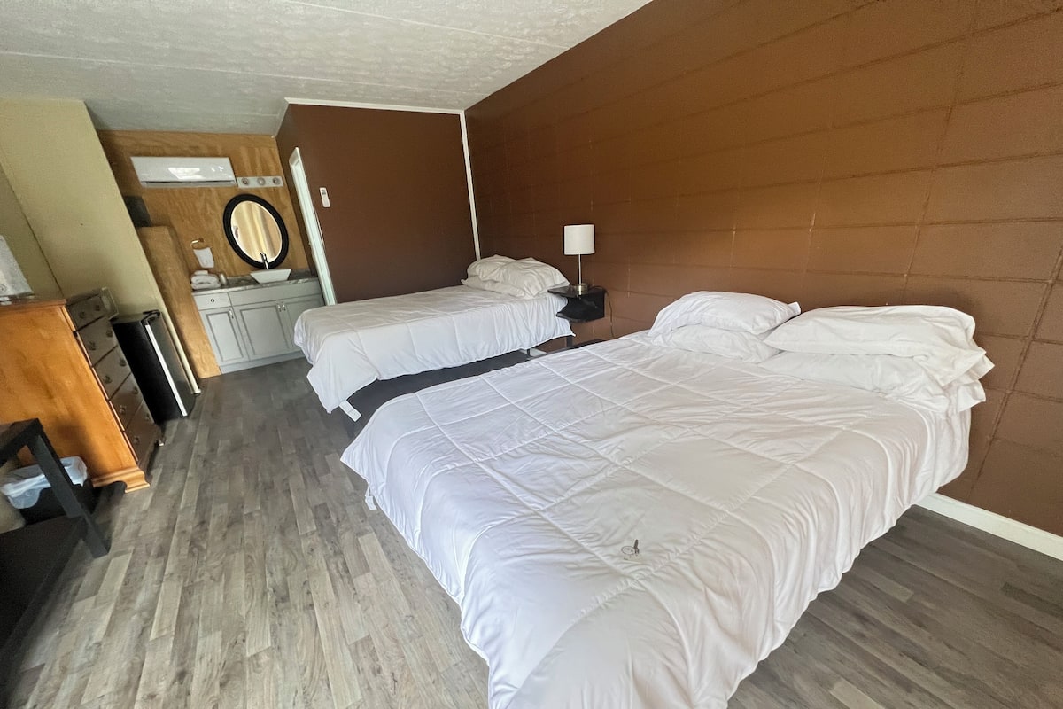 A hotel room with two beds, a wooden dresser, a mirror, and a lamp.