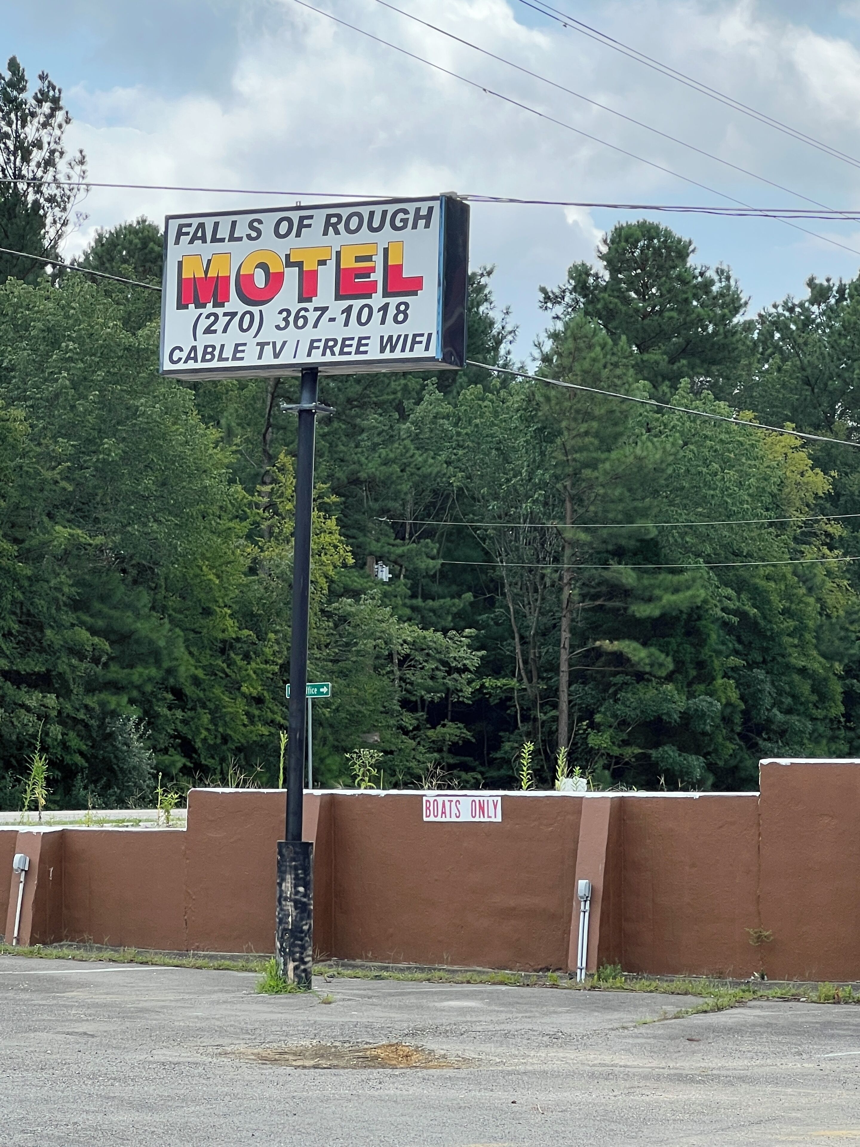 Placa de motel com o nome 'Falls of Rough Hotel' e comodidades como TV a cabo e acesso Wi-Fi gratuito.