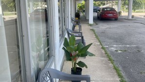 A covered outdoor area with a row of plastic chairs, a potted plant, and a red car parked under a canopy. - Falls of Rough Motel (Falls of Rough)
