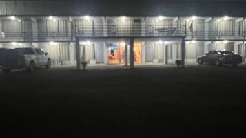 Un edificio de varios pisos, una entrada principal y varios autos estacionados frente a él.