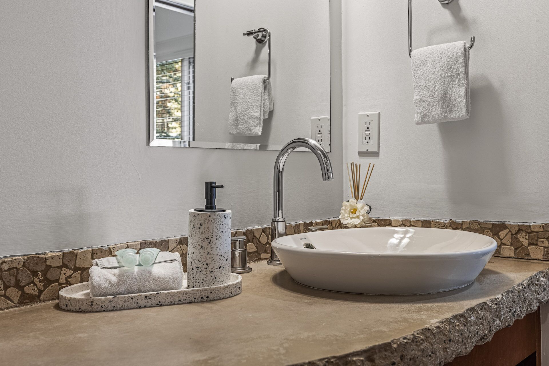 A bathroom with a large sink, a mirror, a towel rack, and a soap dispenser.