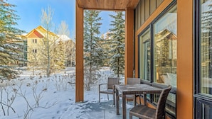 Un espacio de estar al aire libre con techo, muebles de mimbre, suelo cubierto de nieve y vistas de edificios vecinos.