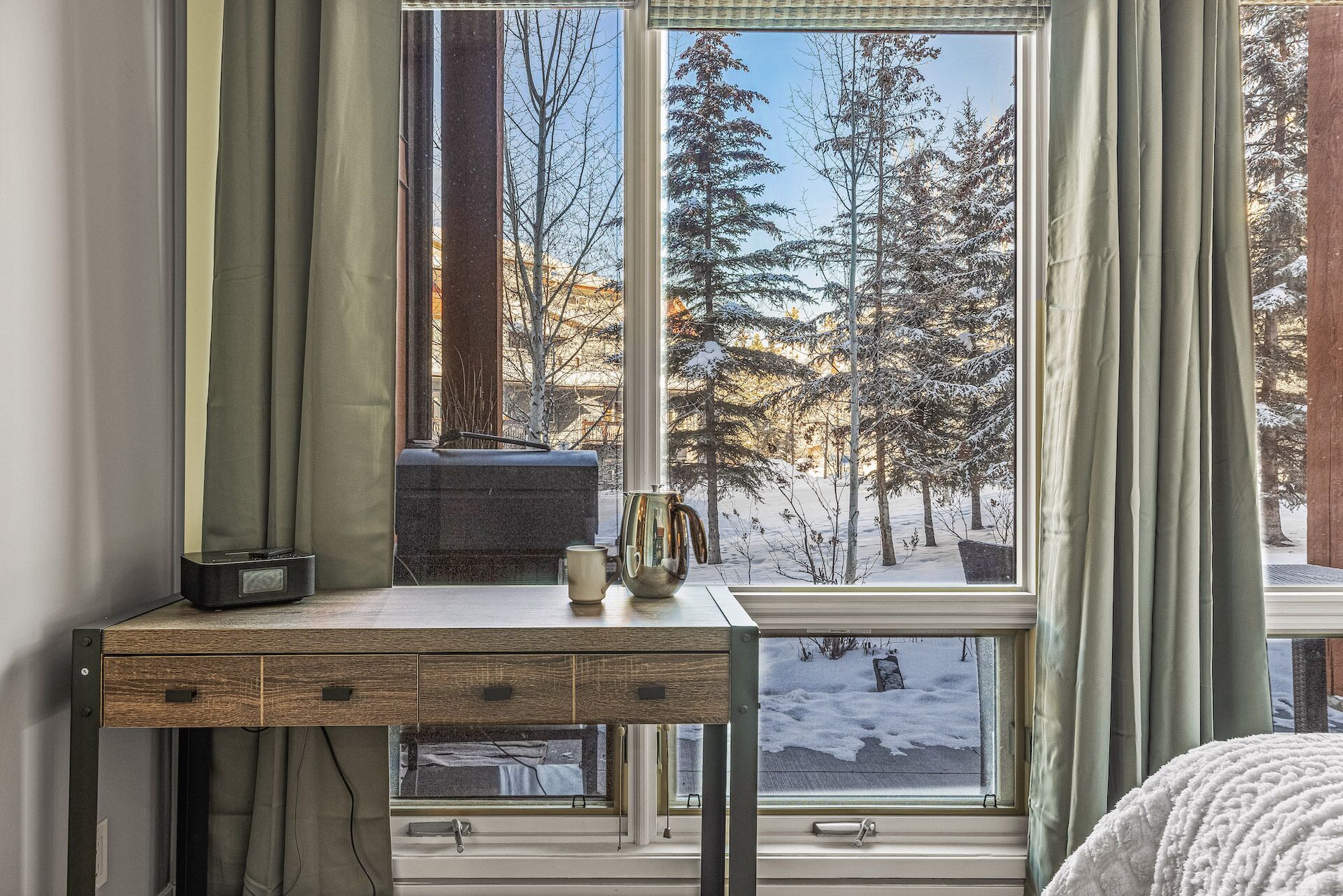 A room with a desk, a window with a view of snow-covered trees, and a window seat.