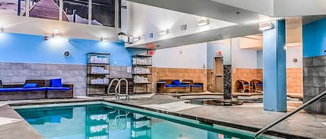 Une piscine avec des chaises longues, un espace sauna et un mur orné d’une horloge.