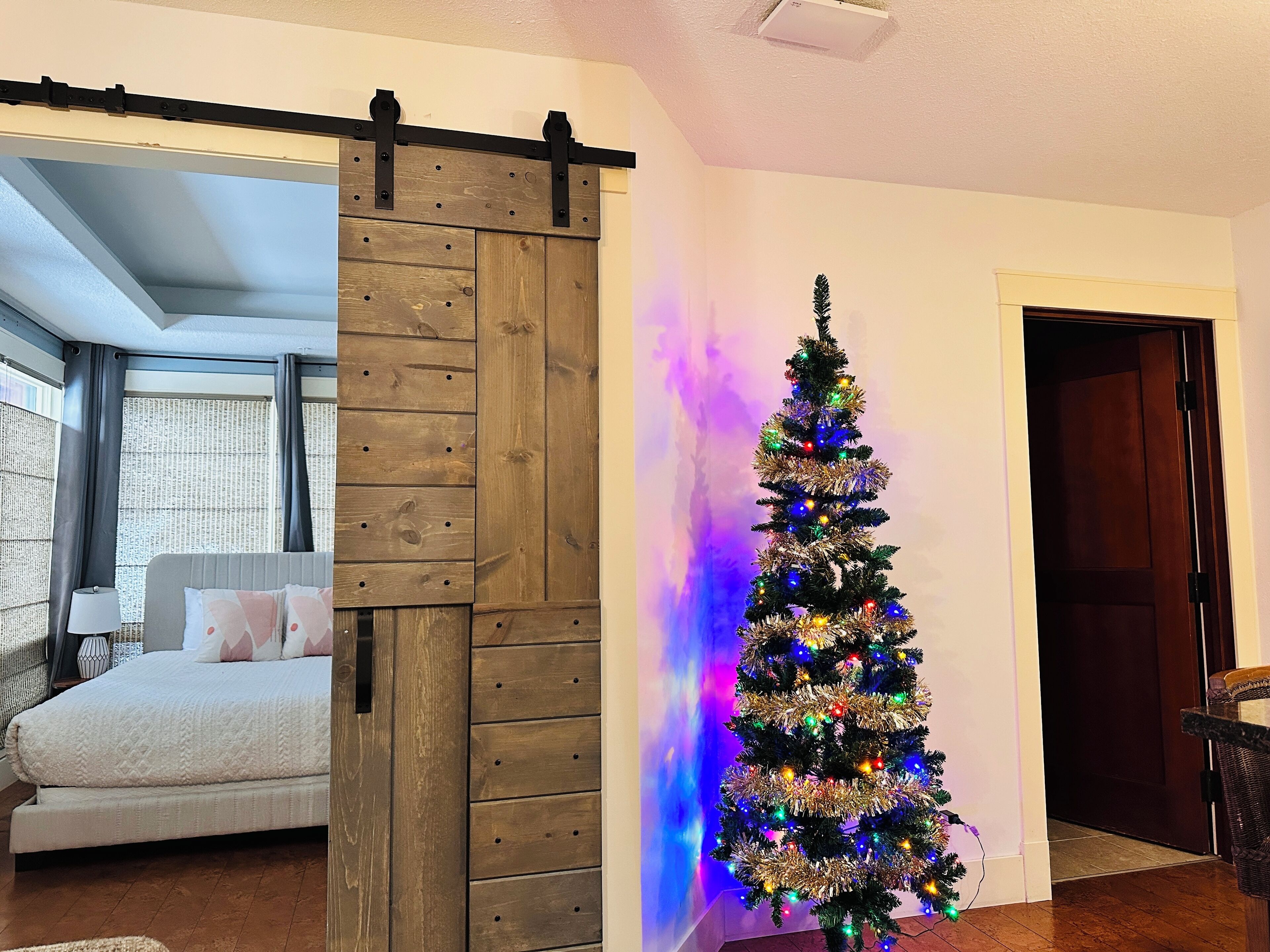 Una habitación con cama, una puerta corrediza de estilo rústico y un árbol de Navidad con luces de colores.