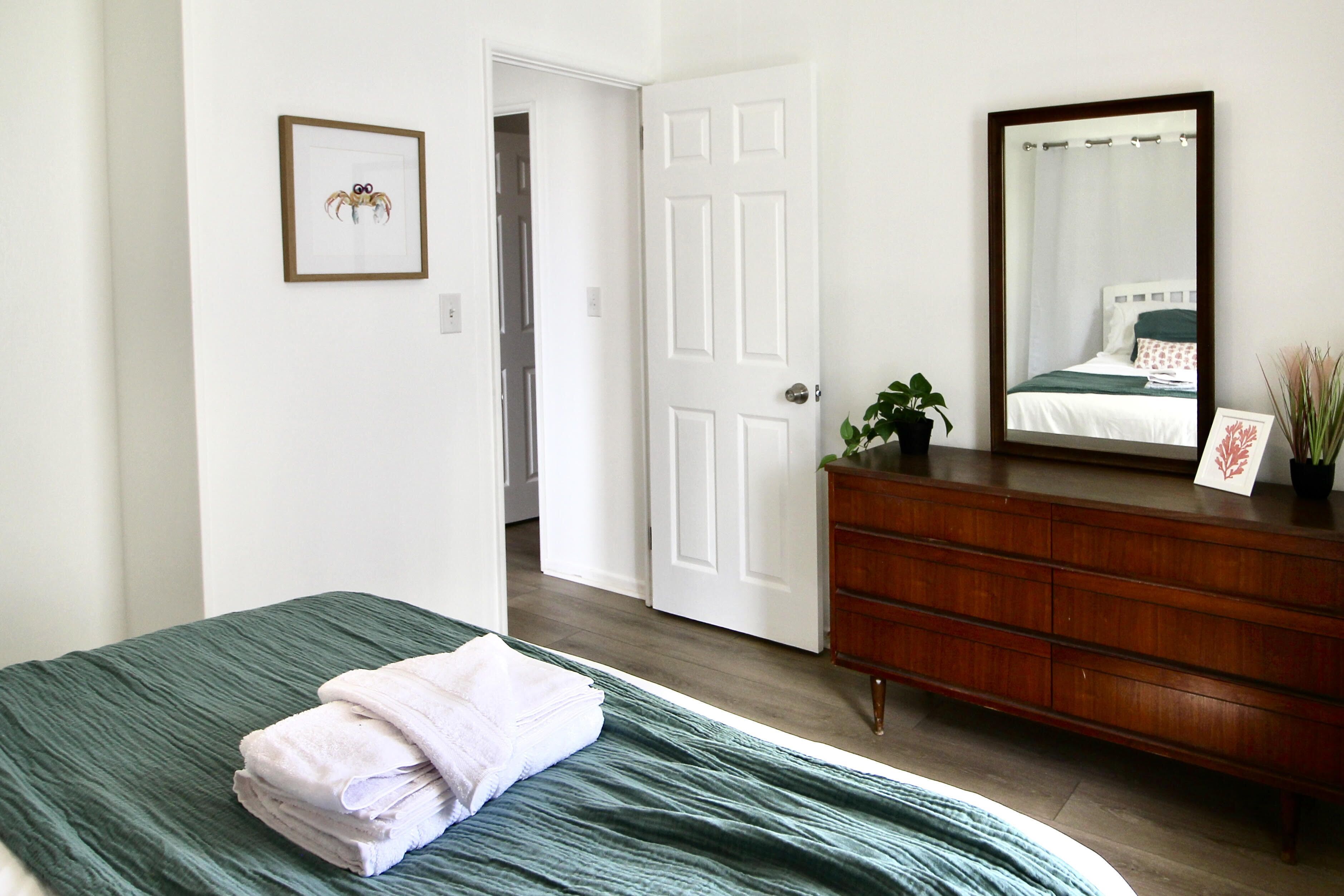 A bedroom with a bed, a dresser, a mirror, and a door leading to another room.