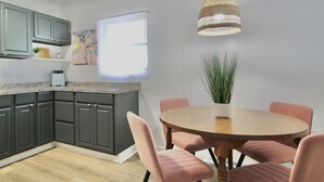 A modern kitchen with grey cabinets, a wooden dining table with pink chairs, and a hanging light fixture. - Relaxing Tropical Getaway! Coral Cottage Melbourne- family and pet friendly home (Melbourne)