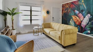 A living room with a sofa, chairs, a small round table, and a large tropical leaf mural on the wall. - Relaxing Tropical Getaway! Coral Cottage Melbourne- family and pet friendly home (Melbourne)