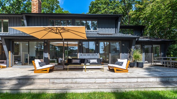 Ein modernes Haus mit einer Terrasse, Gartenmöbeln und einem großen Sonnenschirm.
