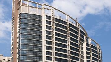 A modern high-rise building with a curved facade, multiple balconies, and a clear sky in the background.