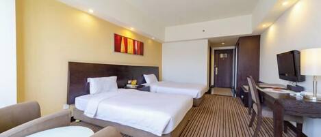 A hotel room with two beds, a desk, a chair, and a TV.