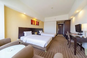 Habitación de hotel con dos camas, un escritorio, una silla y un televisor.
