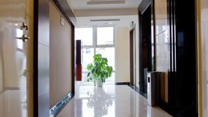 A modern hotel corridor with a shiny floor, a potted plant, and a large window at the end. - Hotel Grand Central (Sihui)