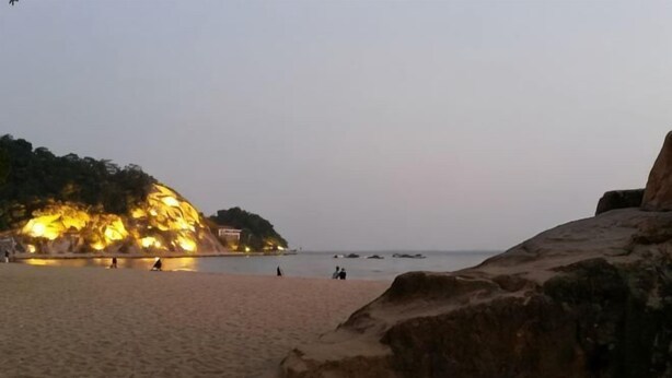 A beach with a rocky outcrop and a building with lights on the left. - Hotel Grand Central (Sihui)