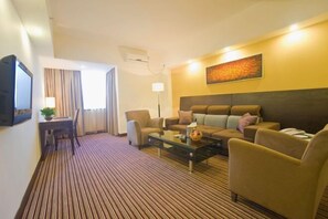 A hotel room with a striped carpet, a sofa set, a coffee table, a TV, and a painting on the wall. - Hotel Grand Central (Sihui)
