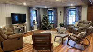 Un vaste salon doté d’un parquet, d’un grand téléviseur à écran plat, d’un sapin de Noël, ainsi que de canapés et de fauteuils en cuir.