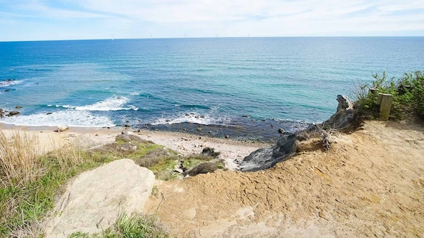 Paisatge costaner amb una platja sorrenca, roques i l'oceà.