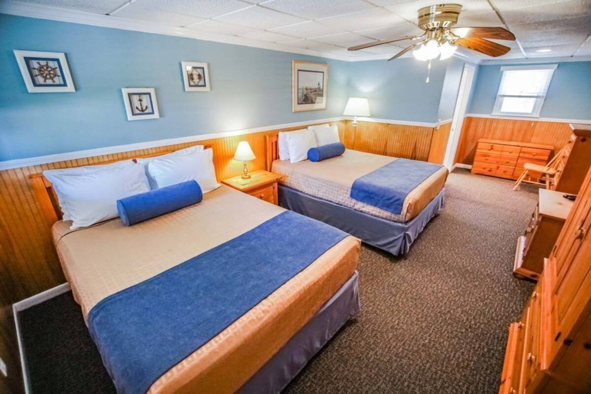 A room with two beds, wooden headboards, a ceiling fan, and a dresser.